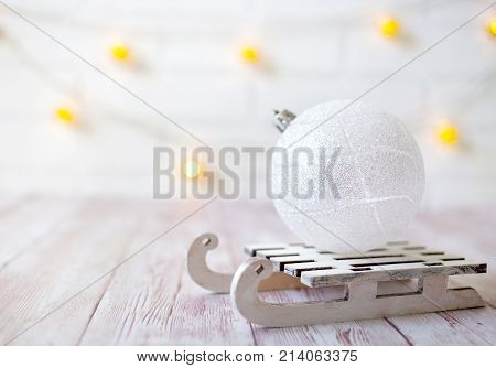 Shining Christmas Ball On Toy Wooden Sled On Light Bokeh Background With Goolden Star. New Year Card