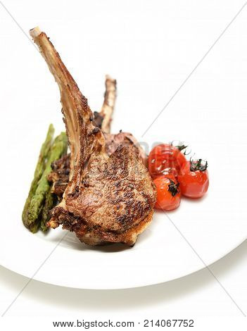 grilled lamb steak with asparagus and tomatoes on a white background