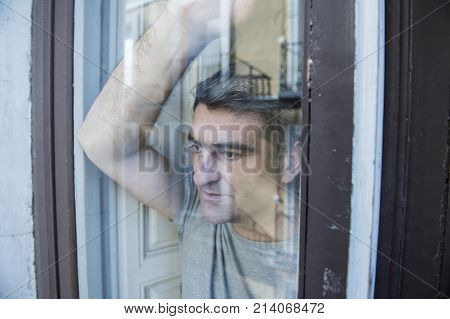 close up portrait of sad and depressed 40s man looking through window glass reflection lonesome and thoughtful suffering depression thinking and feeling low in life crisis and problem concept