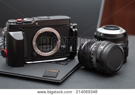 Photographer work desk with mirrorless camera,prime lens, card on laptop on black table in home studio