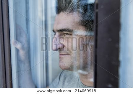 close up portrait of sad and depressed 40s man looking through window glass reflection lonesome and thoughtful suffering depression thinking and feeling low in life crisis and problem concept