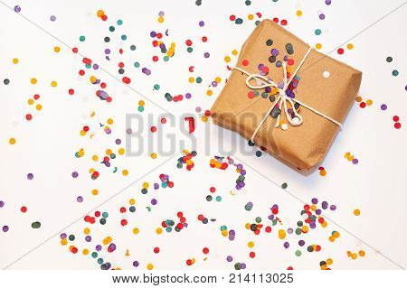 Present box with white bow on white background with multicolored confetti. Flat lay style. Christmas and new year concept