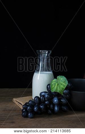 Bottle of milk with grapes and black wowl on wooden floor in still life shot