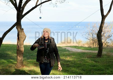 caucasian woman plays with racet and ball in the park. Sea and yachts on the background