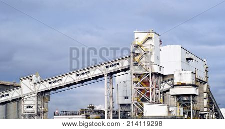a fragment of a modern industrial enterprise with several silos for storage of loose materials and an inclined covered belt conveyor