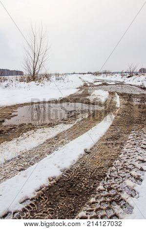 Traces of the tread of the car's wheels on the countryside snow-covered road in the field in the late autumn