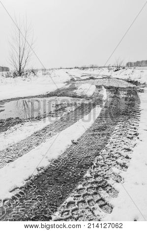 Traces of the tread of the car's wheels on the countryside snow-covered road in the field in the late autumn