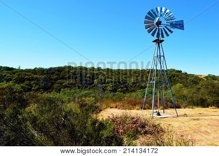 October 15, 2017 in Santa Barbara County, CA:  Vintage rustic windmill surrounded by a rural field of chaparral shrubs taken in the mountains above Santa Barbara, CA where people can buy many acres of rural landscape and ranchland for a reasonable price