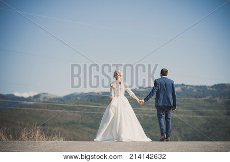 Rear view of happy couple walkin on the road. Holding hands.