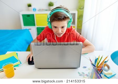 technology, gaming and people concept - boy in headphones playing video game on laptop computer at home