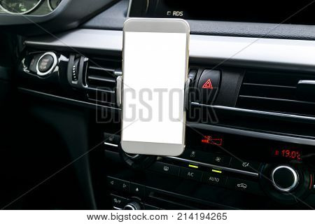 Smartphone in a car use for Navigate or GPS. Driving a car with Smartphone in holder. Mobile phone with isolatede white screen. Blank empty screen. copy space. Empty space for text. modern car interior details.