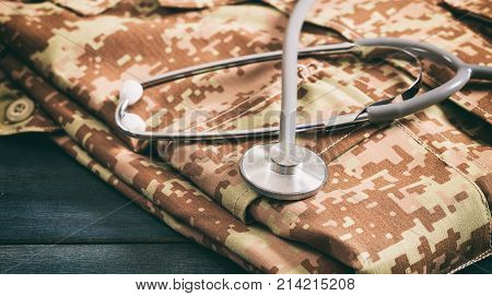 Military medical concept with stethoscope and American military digital pattern uniform folden on wooden background
