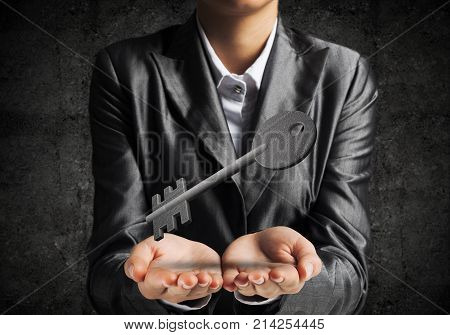 Cropped image of businessman in suit keeping stone key symbol in hands with dark wall on background. 3D rendering.