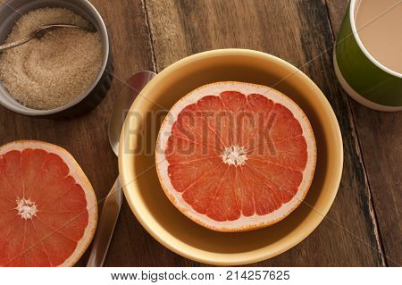 Halved fresh pink or rose grapefruit served in a bowl for breakfast with an accompanying basin of caramelized sugar overhead view