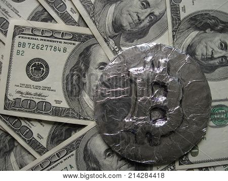Bitcoin real metal coin is on one hundred dollars bills or banknotes. It means hot price or value and high exchange rate of crypto currency on market. It also means investments with financial risk