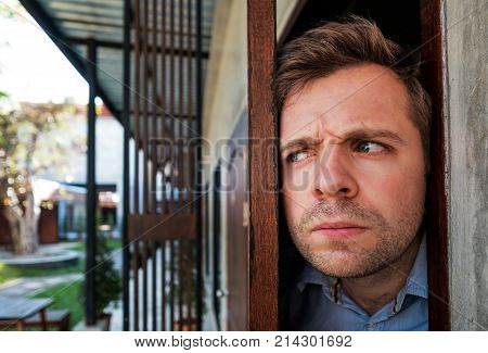 Young caucasian man with agoraphobia spying and looking out the door. He is afraid of communication with people