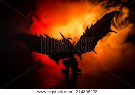 Silhouette Of Fire Breathing Dragon With Big Wings On A Dark Orange Background. Empty Space