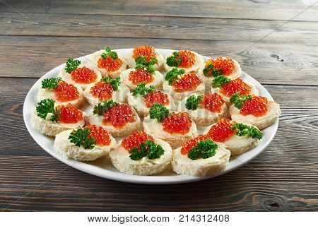 Horizontal shot of red caviar buttered canapes served on the wooden table at the local restaurant eateating food delicious tasty seafood appetizer gourmet delicacy concept.