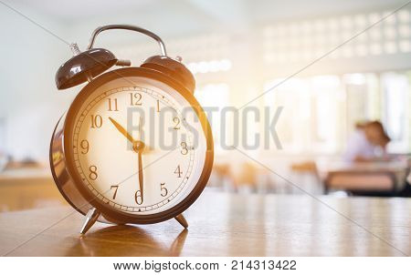 Closeup of Retro alarm clock with ten o'clock on table teacher in blur students exams classroom. Time is indefinite continued progress of existence. Education concept selective focus.