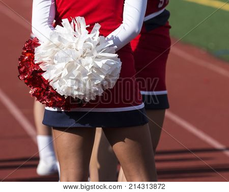 A cheerleader on a sunny afternoon standing with her pom pom behind her.