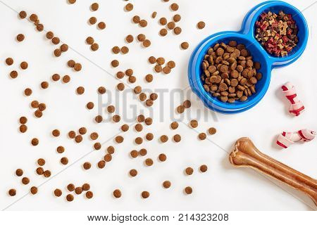 Dry pet food in bowl and bone on white background top view. Copy space. Still life. Flat lay.