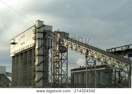 fragment of a modern industrial enterprise with silos for storage of loose materials and an inclined covered belt conveyor