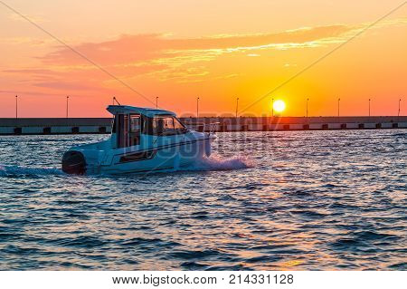 The setting sun over the sea and the motorboat sailing along the mole