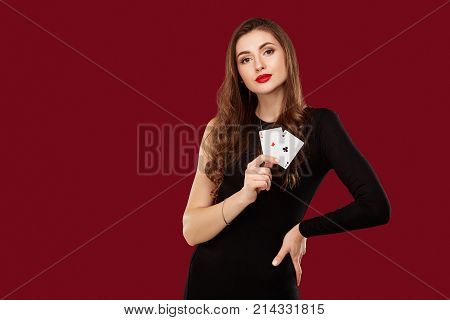 Beautiful caucasian woman in black dress with poker cards gambling in casino. Studio shot on red background. Poker. Two Aces in Hand