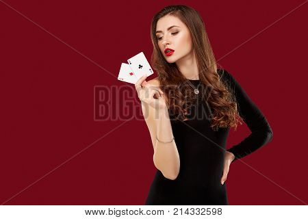 Beautiful caucasian woman in black dress with poker cards gambling in casino. Studio shot on red background. Poker. Two Aces in Hand
