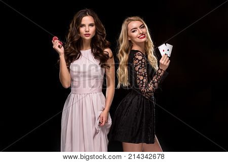 Two Sexy girls brunette and blonde, posing with chips and cards in their hands, poker concept. Studio shot. Two beautiful women in dresses on a black background