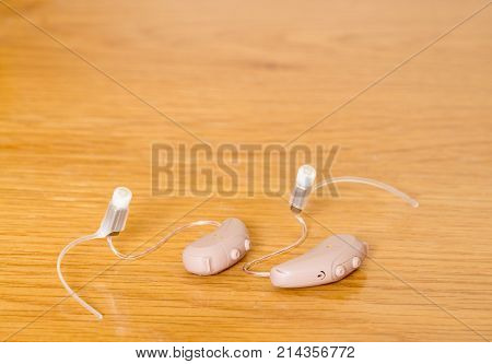 Macro close up of a matched pair of tiny modern hearing aid on wooden bedside dressing table