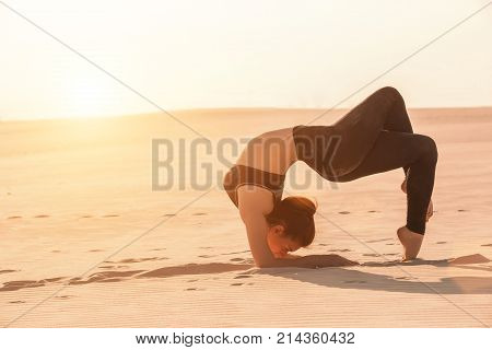 Fitness yoga woman stretching on sand. Fit female athlete doing yoga pose before running training outside in amazing landscape.