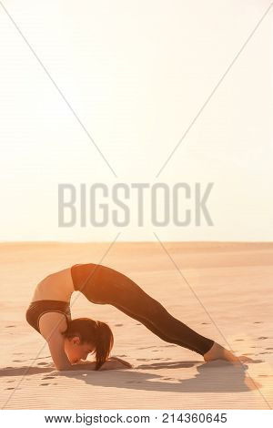 Fitness yoga woman stretching on sand. Fit female athlete doing yoga pose before running training outside in amazing landscape.