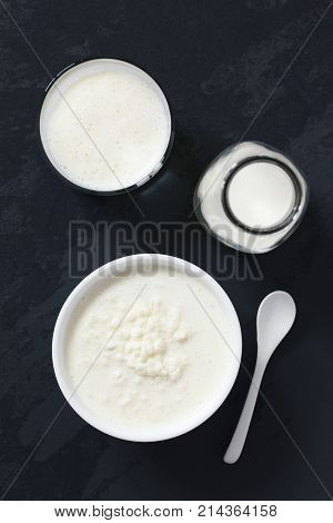 Kefir grains in milk with bottle of milk and a glass of fresh kefir drink on the side photographed overhead on slate with natural light (Selective Focus Focus on the top of the kefir grains and the kefir drink)