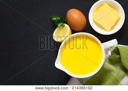 Hollandaise sauce a basic sauce of the French cuisine served in a sauce boat with ingredients (egg butter lemon) on the side photographed overhead on slate with natural light