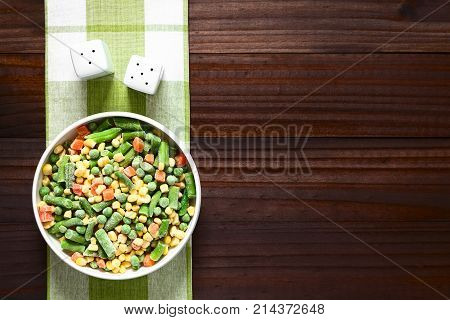 Frozen mixed vegetables (green bean pea carrot sweet corn) in bowl photographed overhead on dark wood with natural light