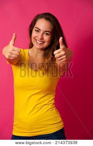 Cute Young Woman In Yellow T Shirt Smiling Over Pink Background Showing Thumbs Up As A Hesture Of Su