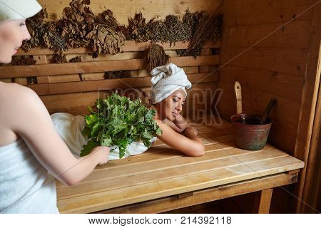 two beautiful young women in towels realxing in wooden sauna. inside shot with natural light.