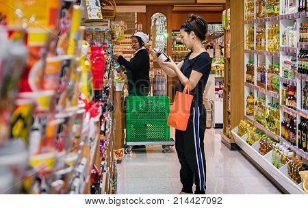 BANGKOK THAILAND - NOVEMBER 02: A female customer reads the label on a bottle of sauce in the sauce section in Foodland suppermarket in Bangkok on November 02 2017.