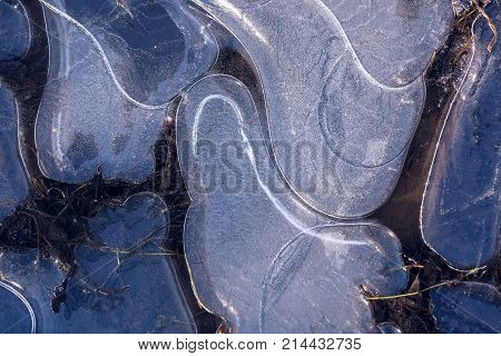 Beautiful winter background with a pattern of thin ice on a puddle in the form of different shapes in the sunlight