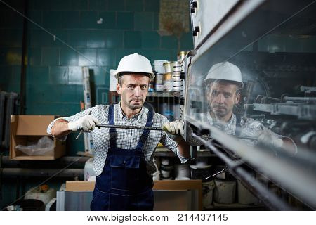 Worker in overall and harhat repairing industrial equipment