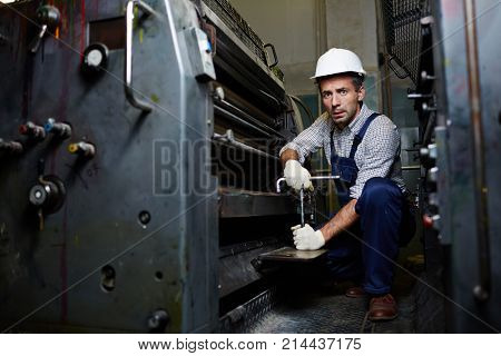 Engineer with handtool doing his work by huge industrial machine in factory