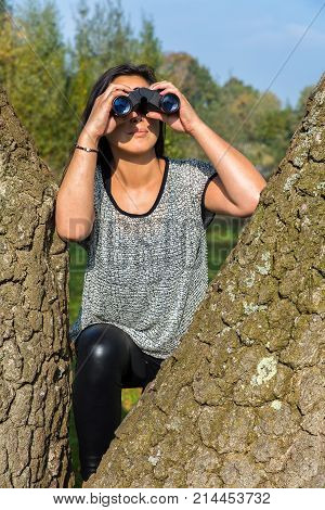 Young woman looking through binoculars between tree trunks
