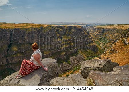 Young woman sitting on the edge of Kasagh river gorge near Saghmosavank monastery