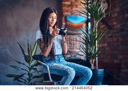 Tattooed brunette amateur female photographer takes pictures in a room with loft interior.