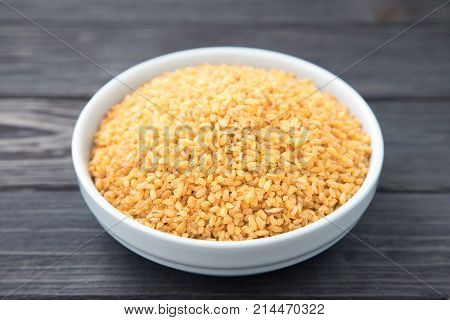 Uncooked Bulgur In Blue Bowl On Wooden Table Background. Dry Bulgur. Spilled Bulgur