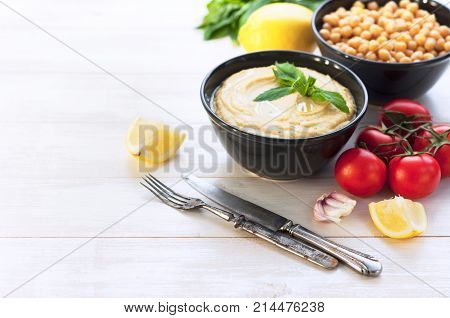 Bowl with hummus, chickpeas, lemon, cherry tomatoes and herbs on a white rustic wooden background.
Middle Eastern cuisine. Background hummus with place for text.