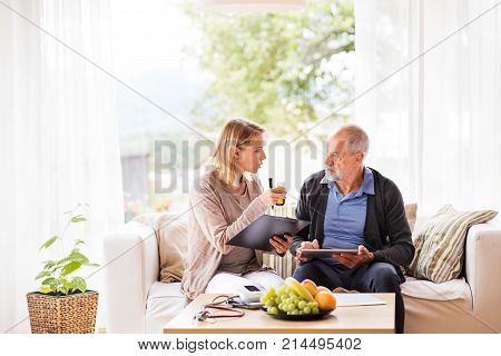 Health visitor and a senior man during home visit. A female nurse or a doctor showing test results on a tablet.