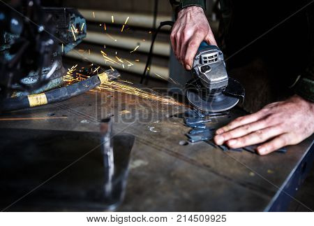 Engineer polish metal product with electric grinder tool.Specialist polishes steel blank with abradive polishing disc at workshop.Metal shop work process at factory.Specialist works with grinder