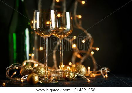 Two glasses for wine and golden Christmas balls against a background of blurred golden lights. Shallow depth of field.